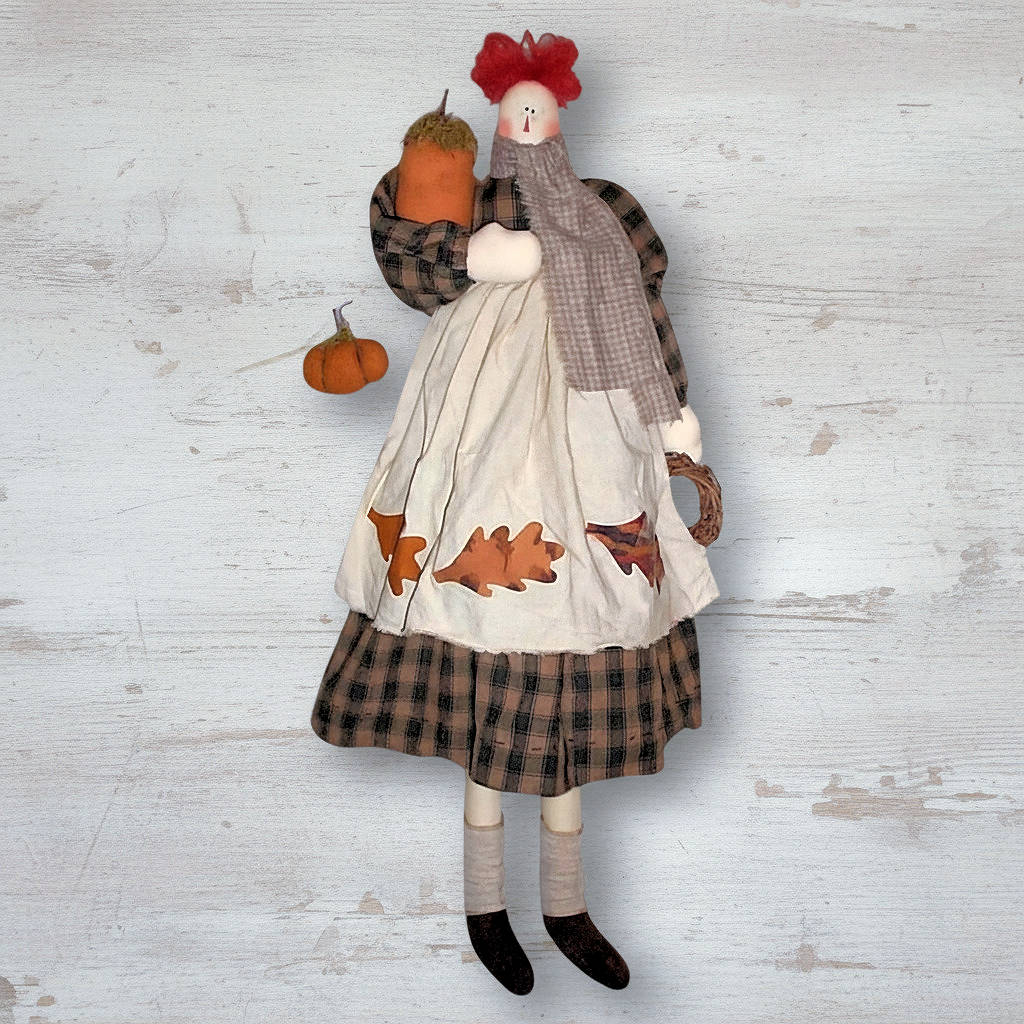 Decorative doll with plaid outfit and pumpkins on a textured white background