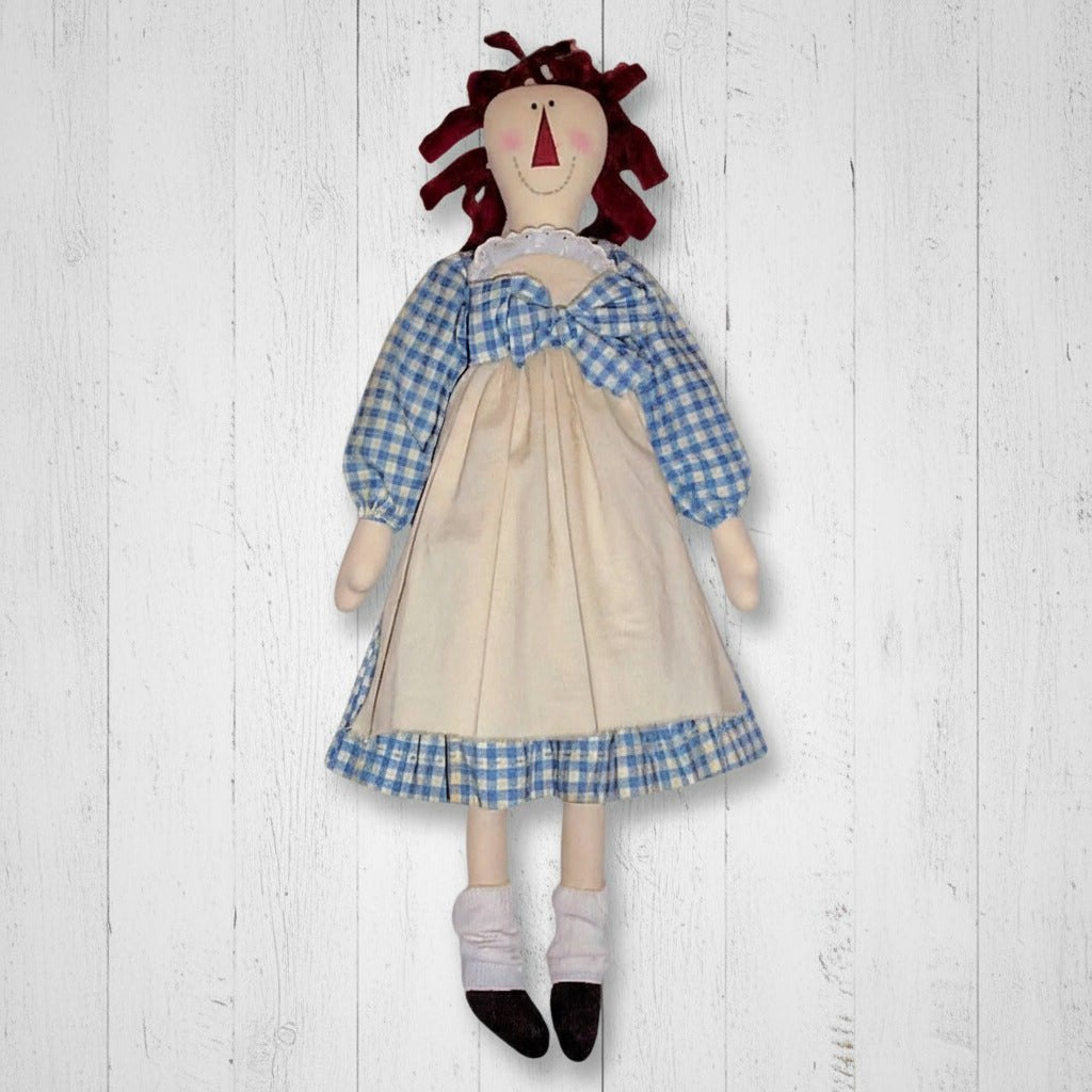Textile doll with a blue checkered top and beige skirt on a white background