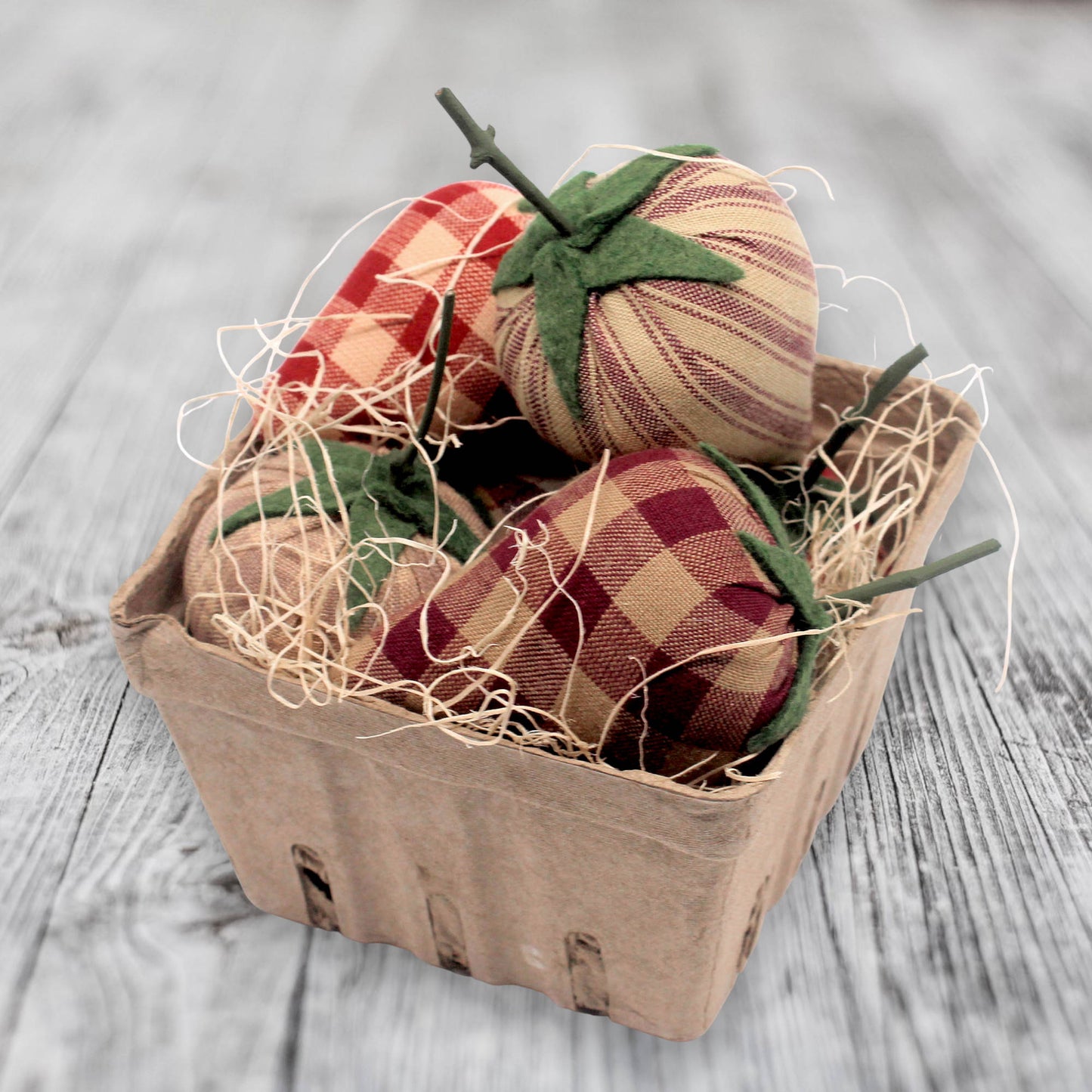 Decorative fabric strawberries in a cardboard box on a wooden surface