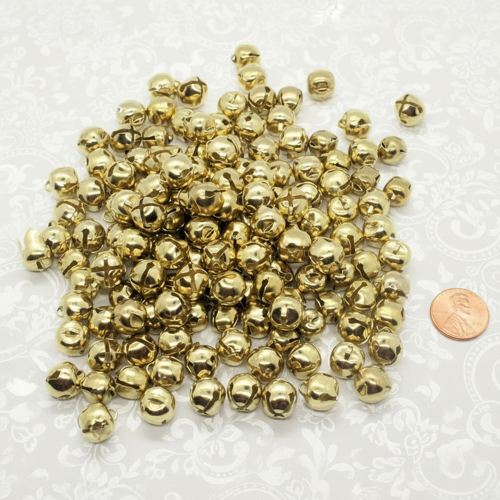 Gold jingle bells with a penny for scale on a white background