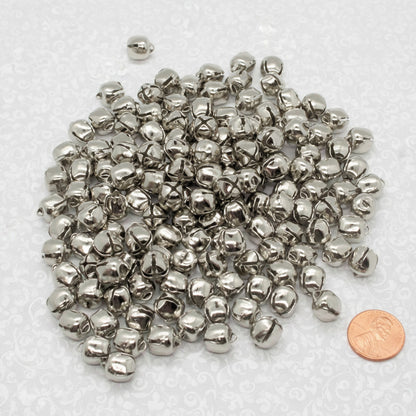 Pile of small metal silver jingle bells with a penny for scale on a white background
