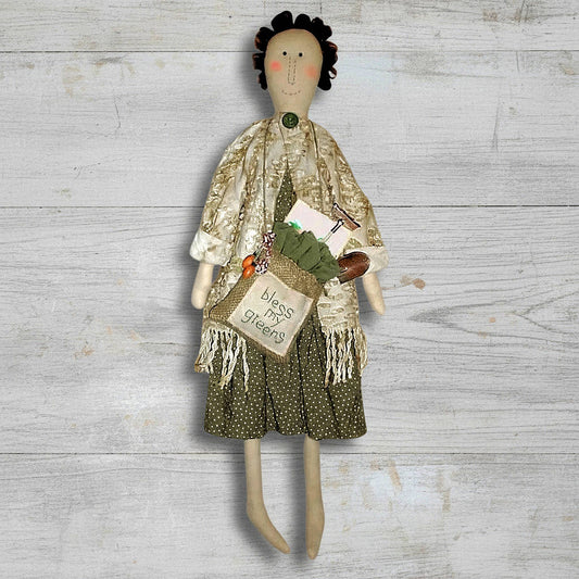 Textile doll with a green dress and white jacket on a wooden surface