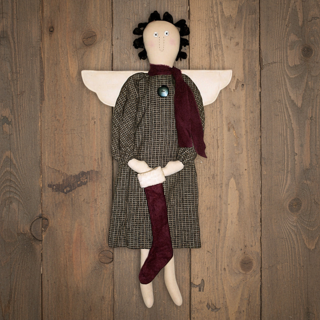 Textile angel figurine with plaid dress and maroon scarf against a wooden background