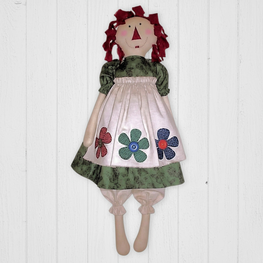 Handmade doll with red hair, floral dress, and green apron on a white background