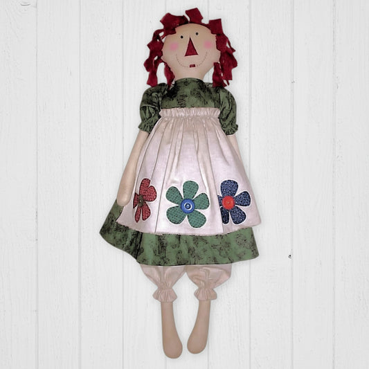 Handmade doll with red hair, floral dress, and green apron on a white background