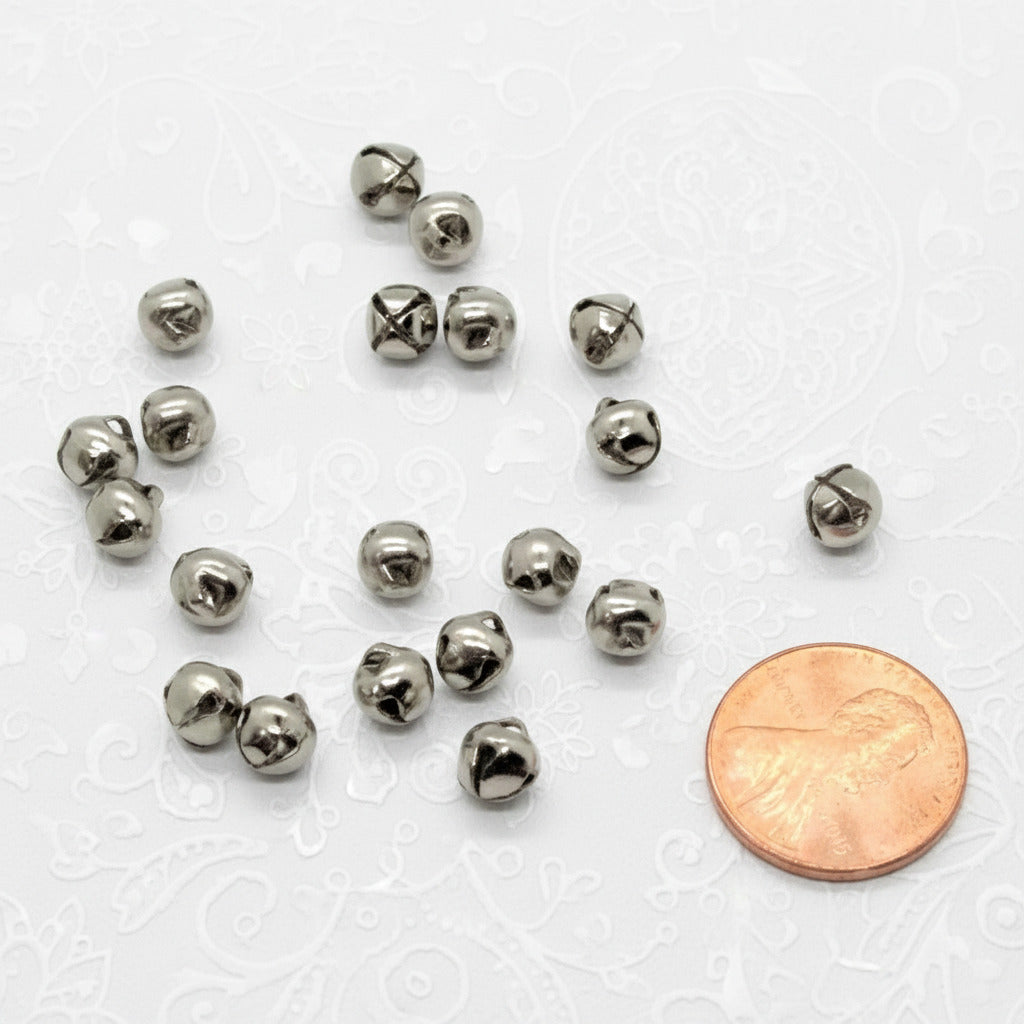 Small silver jingle bells with a penny for scale on a white background
