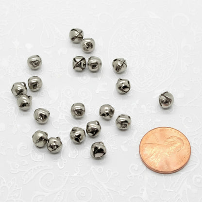 Small silver jingle bells with a penny for scale on a white background