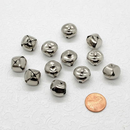 Silver jingle bells with a penny for scale on a white background