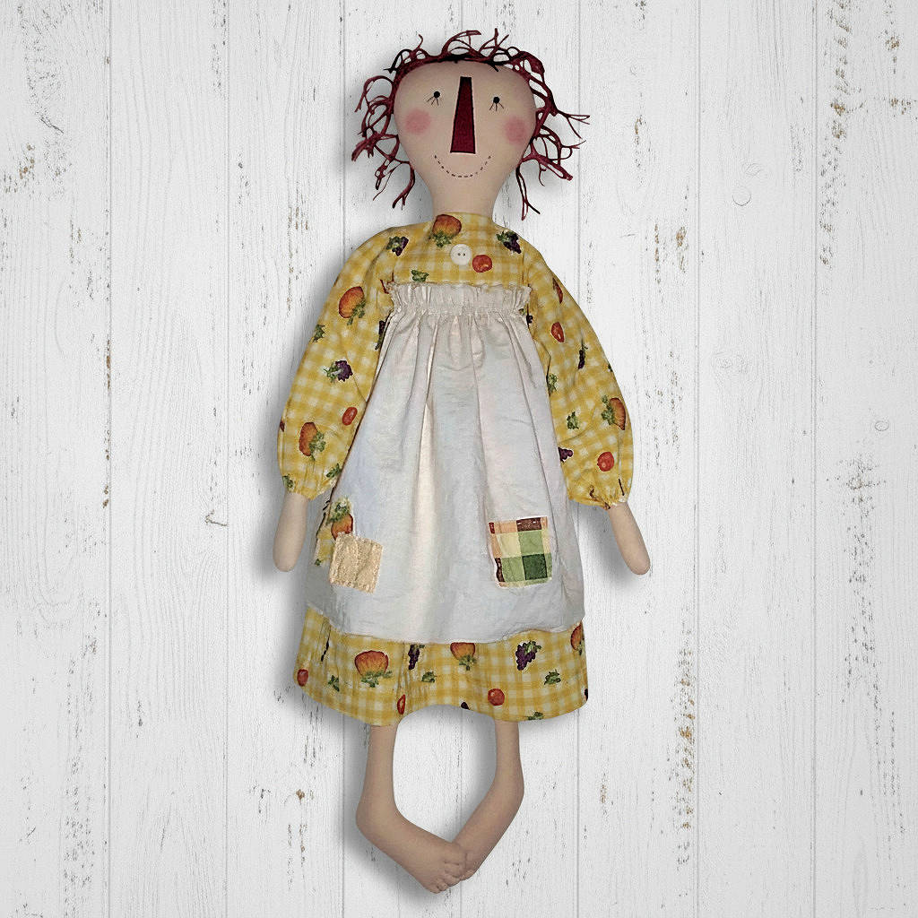Textile doll with a yellow dress and white apron on a wooden background
