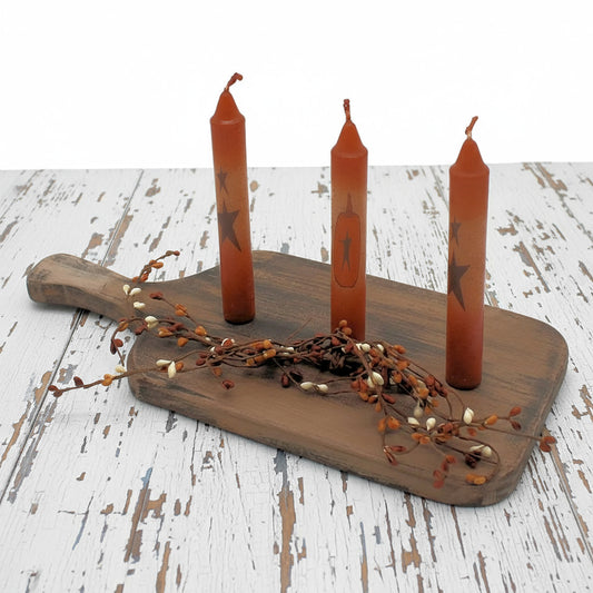 Wooden cutting board with three orange candles and decorative branches on a white background