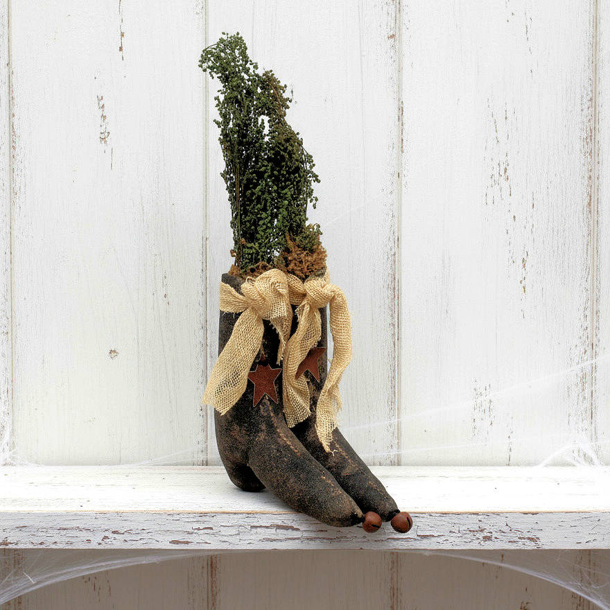 Decorative pair of rustic witch boots with dried plants and a bow on a white wooden surface.