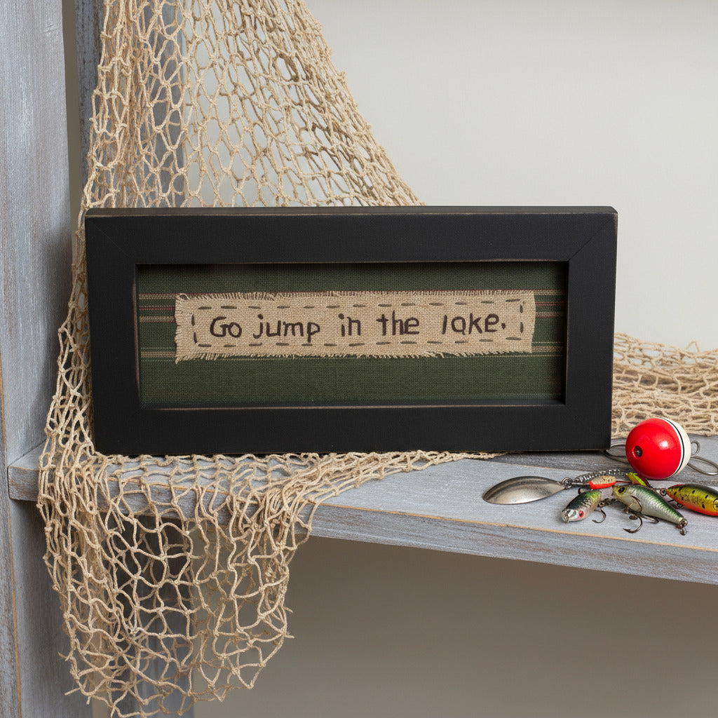 Framed quote 'Go jump in the lake' on a shelf with fishing net and accessories.