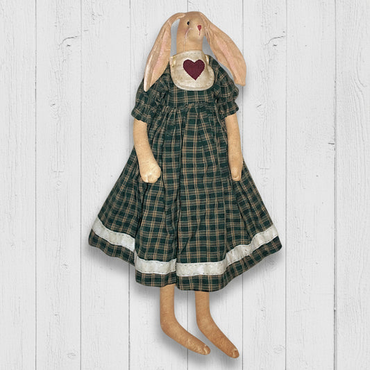 Stuffed bunny toy wearing a green plaid dress with a heart on a white background