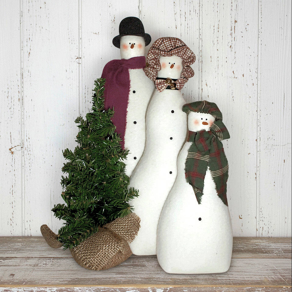 Three snowman dolls with scarves and a small tree on a wooden surface.