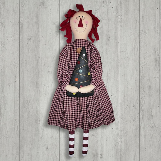 Vintage-style doll with red hair, checkered dress, and striped socks holding a black cone-shaped object on a wooden background.