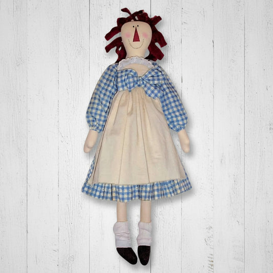 Textile doll with a blue checkered top and beige skirt on a white background