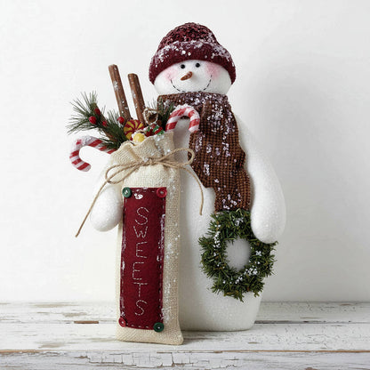 Decorative snowman figurine with a red sack labeled 'Sweets', candy canes, and a wreath on a white background.