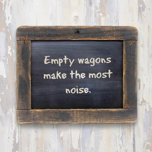 Chalkboard with text 'Empty wagons make the most noise.' on a wooden frame against a rustic wall.