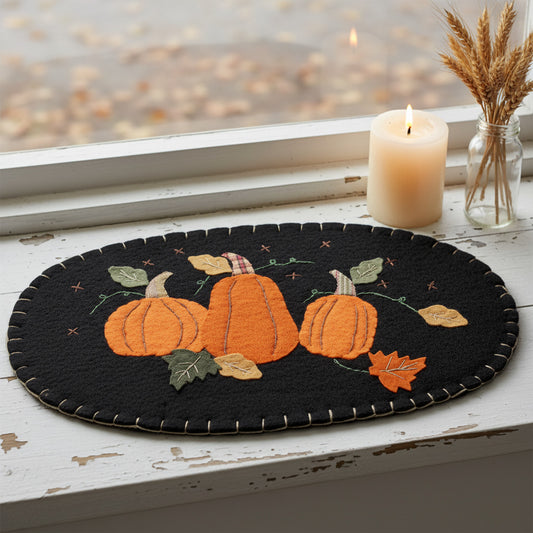 Decorative black oval mat with orange pumpkins and autumn leaves on a white background