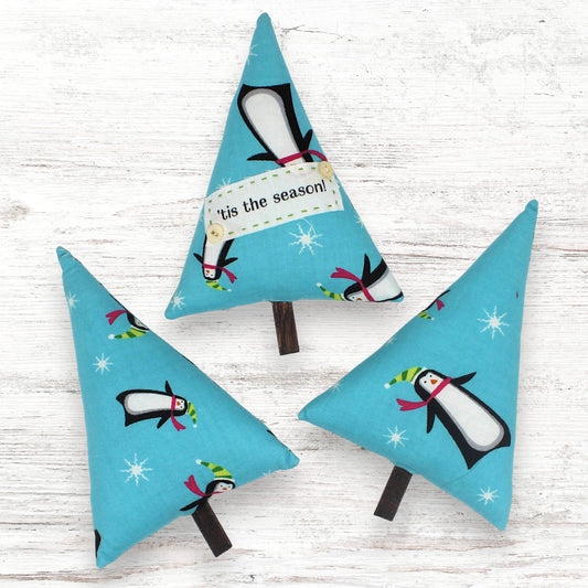 Three tree-shaped bowl fillers with penguin designs on a light wooden surface