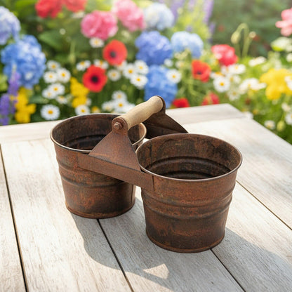 Rustic metal double planter on a wooden surface with a colorful flower garden in the background