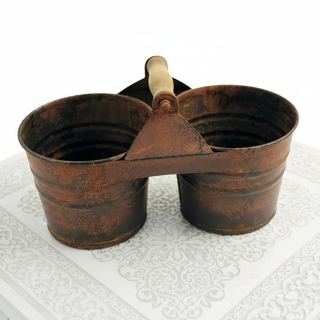 Rustic metal double bucket with wooden handle on a textured white surface