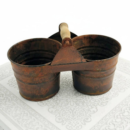 Rustic metal double bucket with wooden handle on a textured white surface