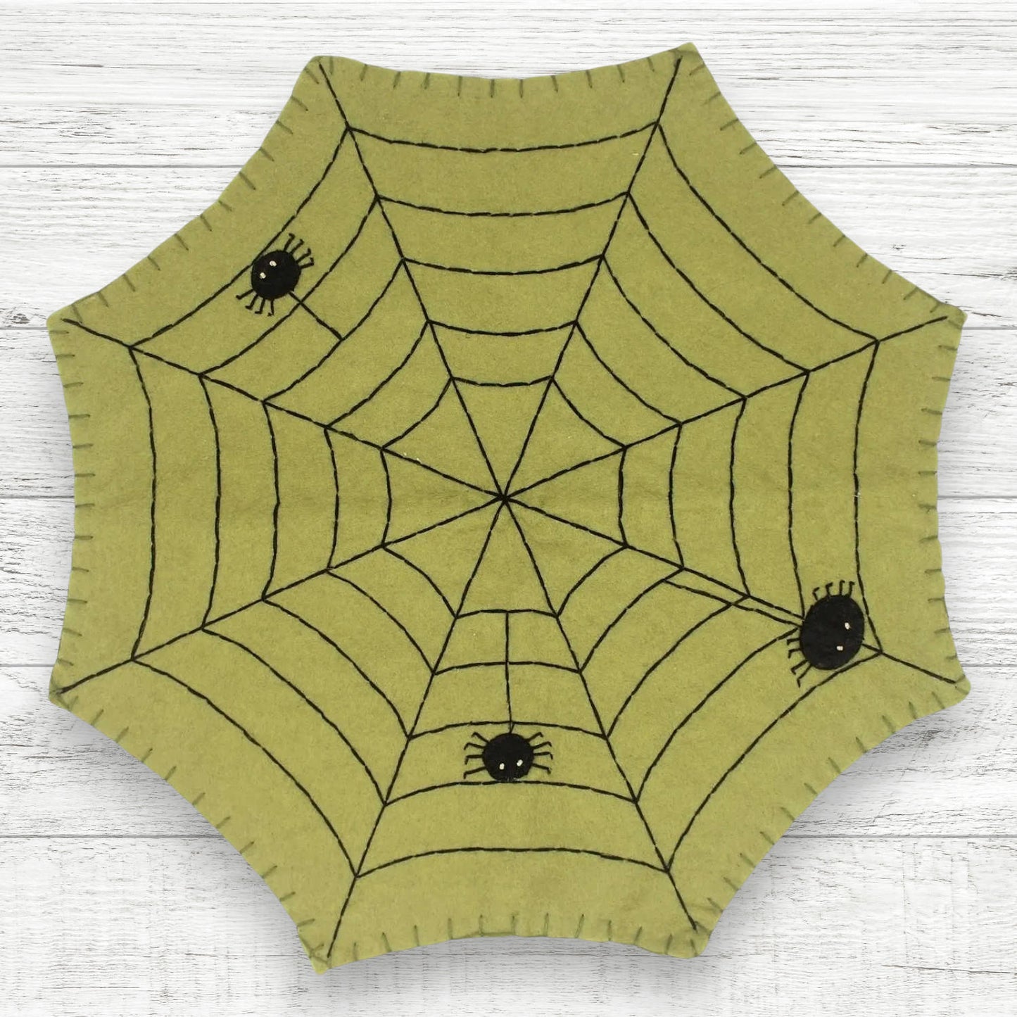 Hexagonal green fabric with spider web design on a white wooden surface