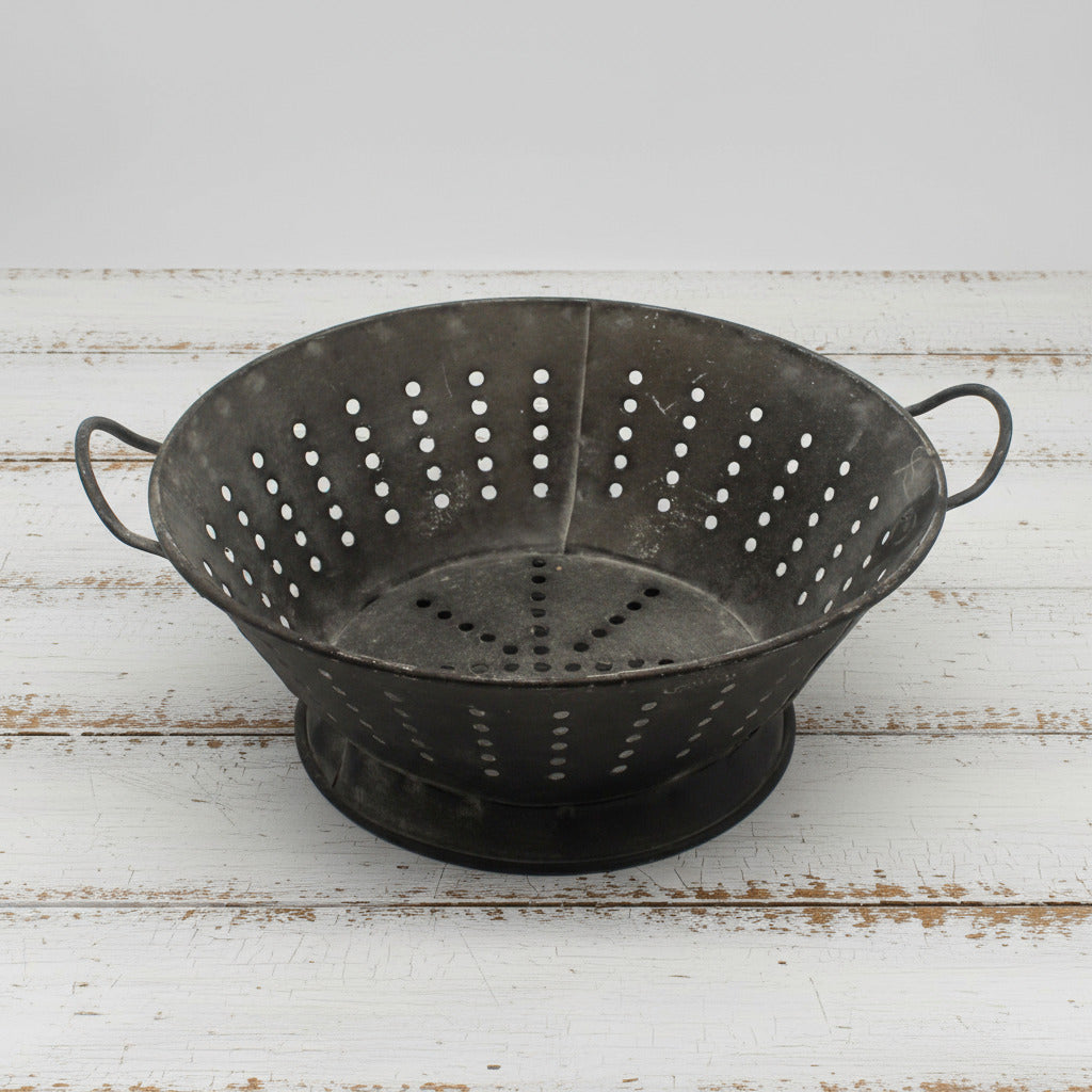 Highly distressed decorative metal colander on a white background