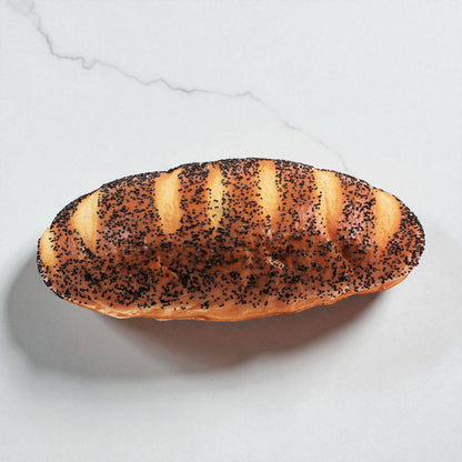 Fake decorative loaf of bread with poppy seeds on a light gray surface
