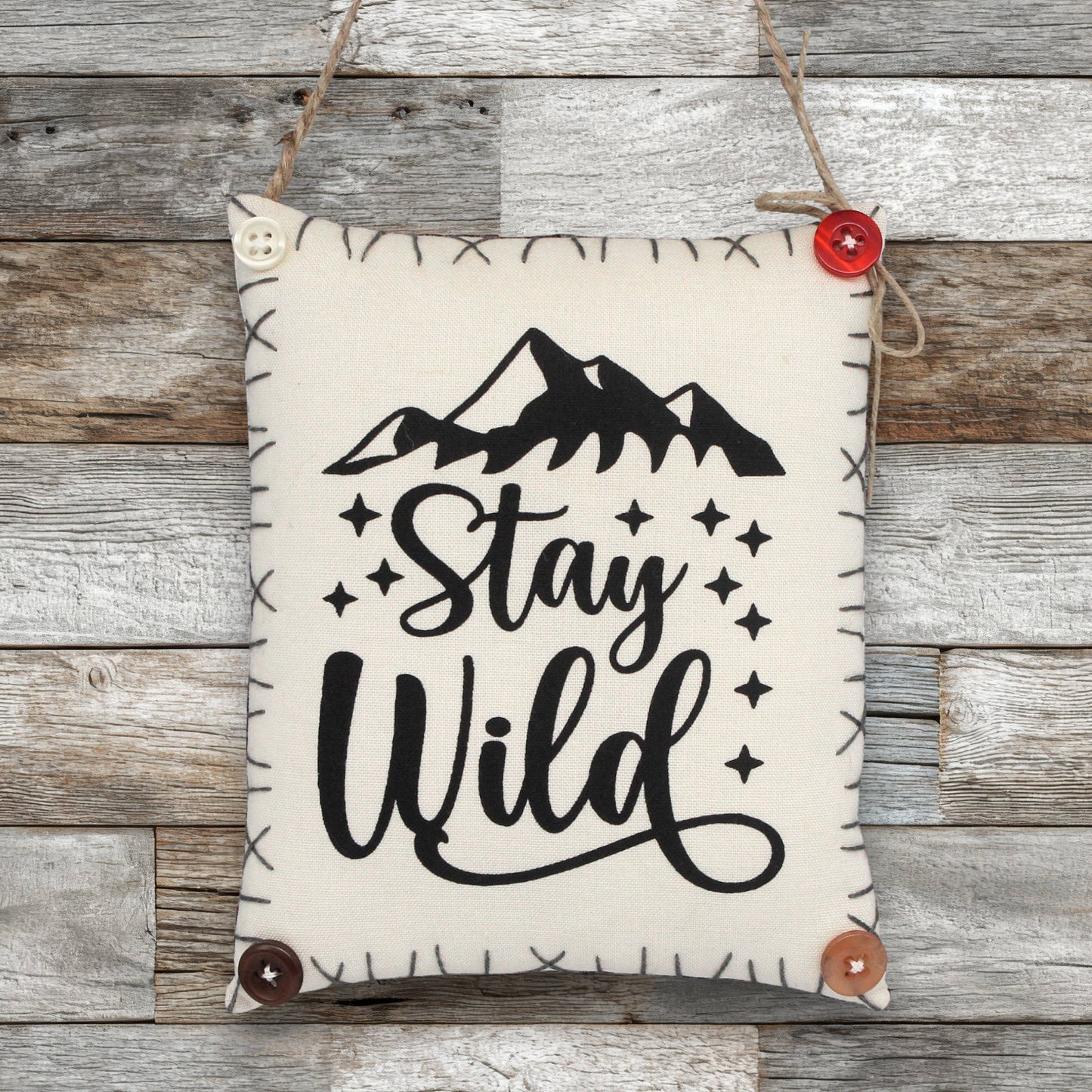 Fabric sign ornament with 'Stay Wild' text and mountain graphic on a wooden background