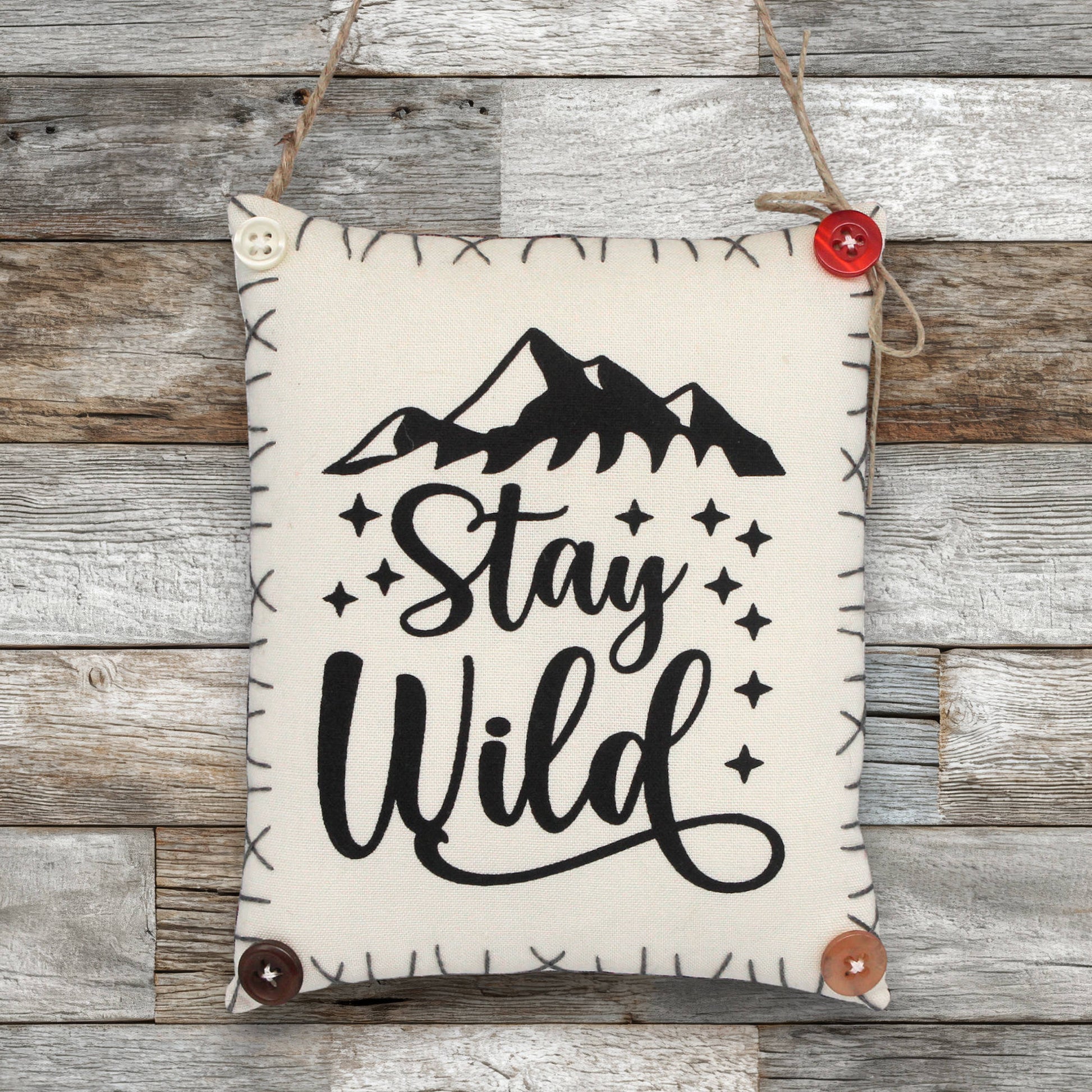 Fabric sign ornament with 'Stay Wild' text and mountain graphic on a wooden background