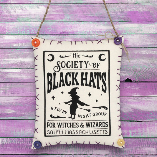 Decorative sign ornament with 'The Society of Black Hats' text and witch silhouette on a wooden background.
