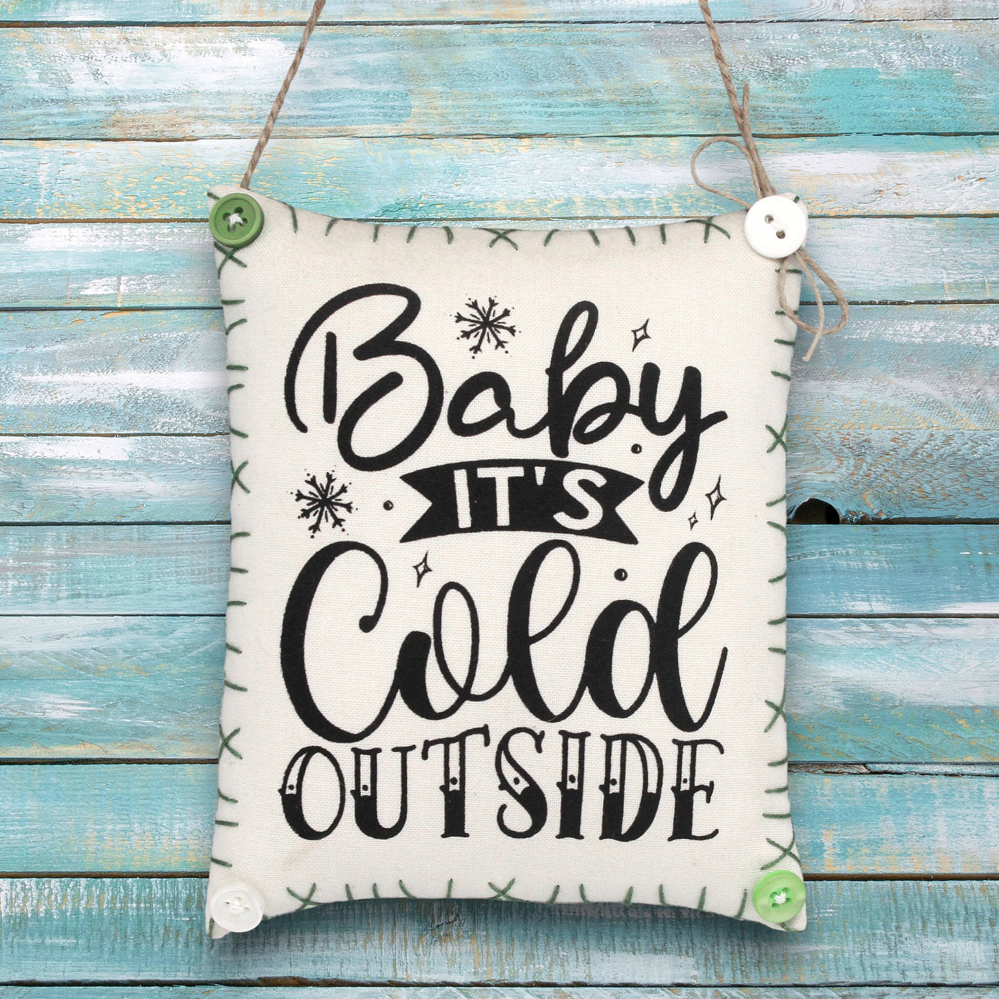 Fabric sign ornament with 'Baby It's Cold Outside' text on a wooden background