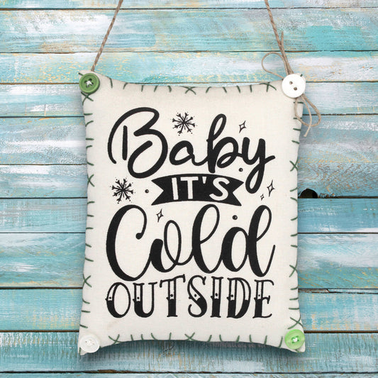 Fabric sign ornament with 'Baby It's Cold Outside' text on a wooden background