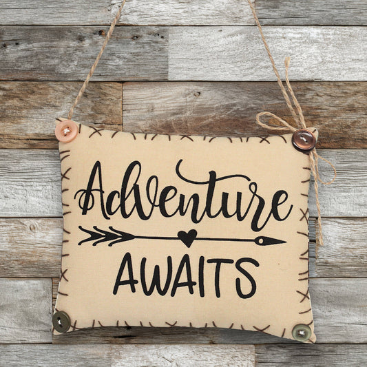Sign ornament with 'Adventure Awaits' text on a wooden background