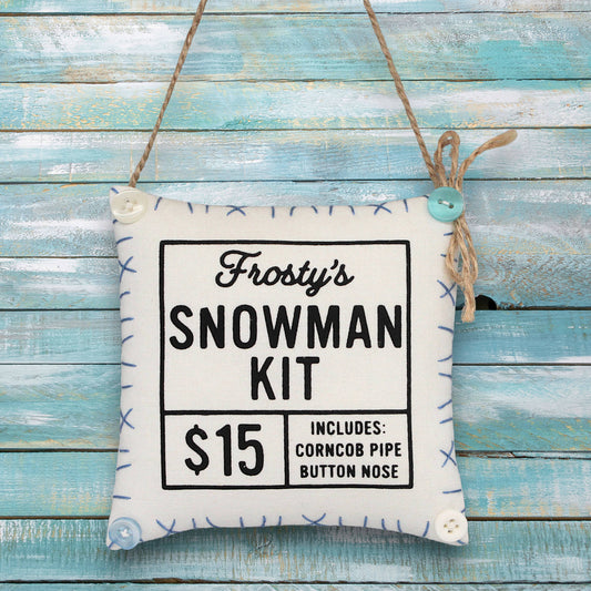 Fabric sign ornament for 'Frosty's Snowman Kit' on a wooden background