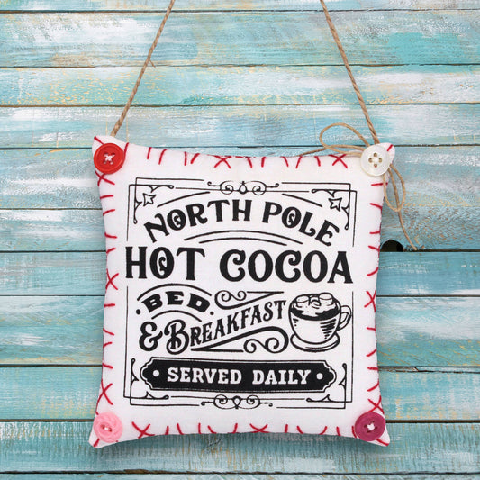 Decorative sign ornament with 'North Pole Hot Cocoa Bed & Breakfast' text on a wooden background