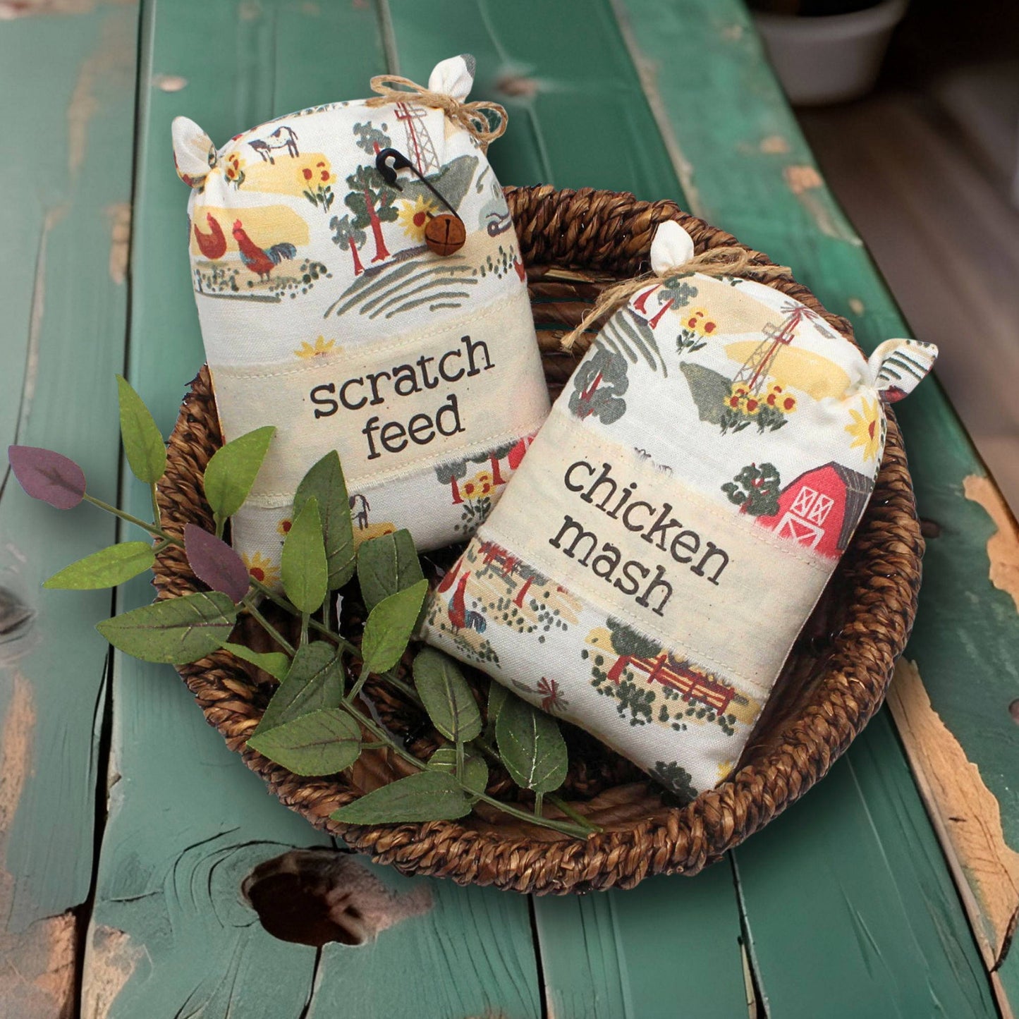 Two decorative grain sack bowl fillers labeled 'scratch feed' and 'chicken mash' in a woven basket on a wooden surface.