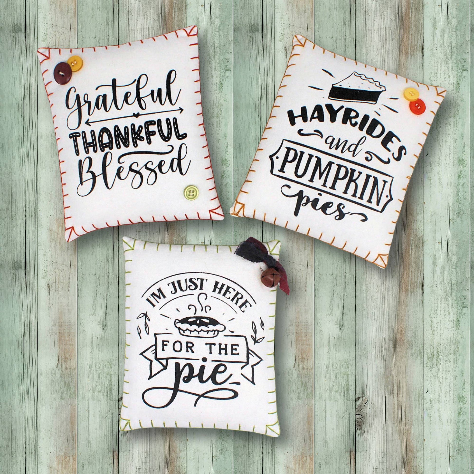 Three decorative pillows with autumn-themed sayings on a wooden background