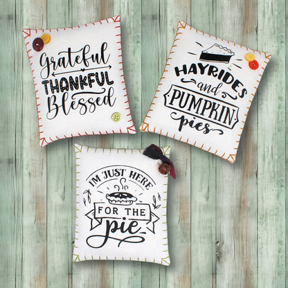 Three decorative pillows with autumn-themed sayings on a wooden background