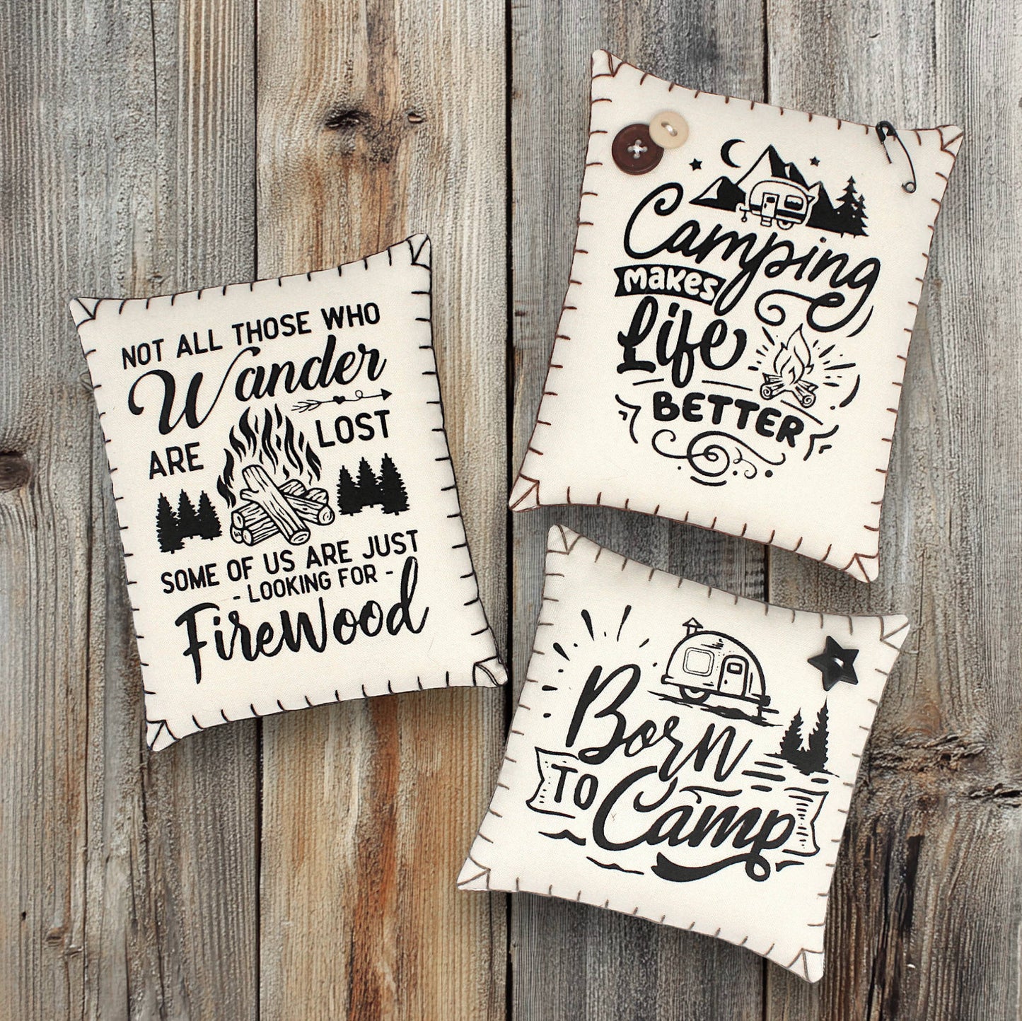 Three decorative pillows with camping-themed text on a wooden background