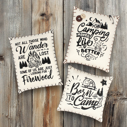 Three decorative pillows with camping-themed text on a wooden background