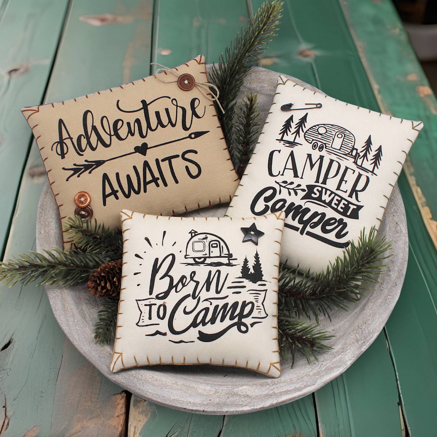 Three decorative pillows with camping-themed text on a wooden surface.