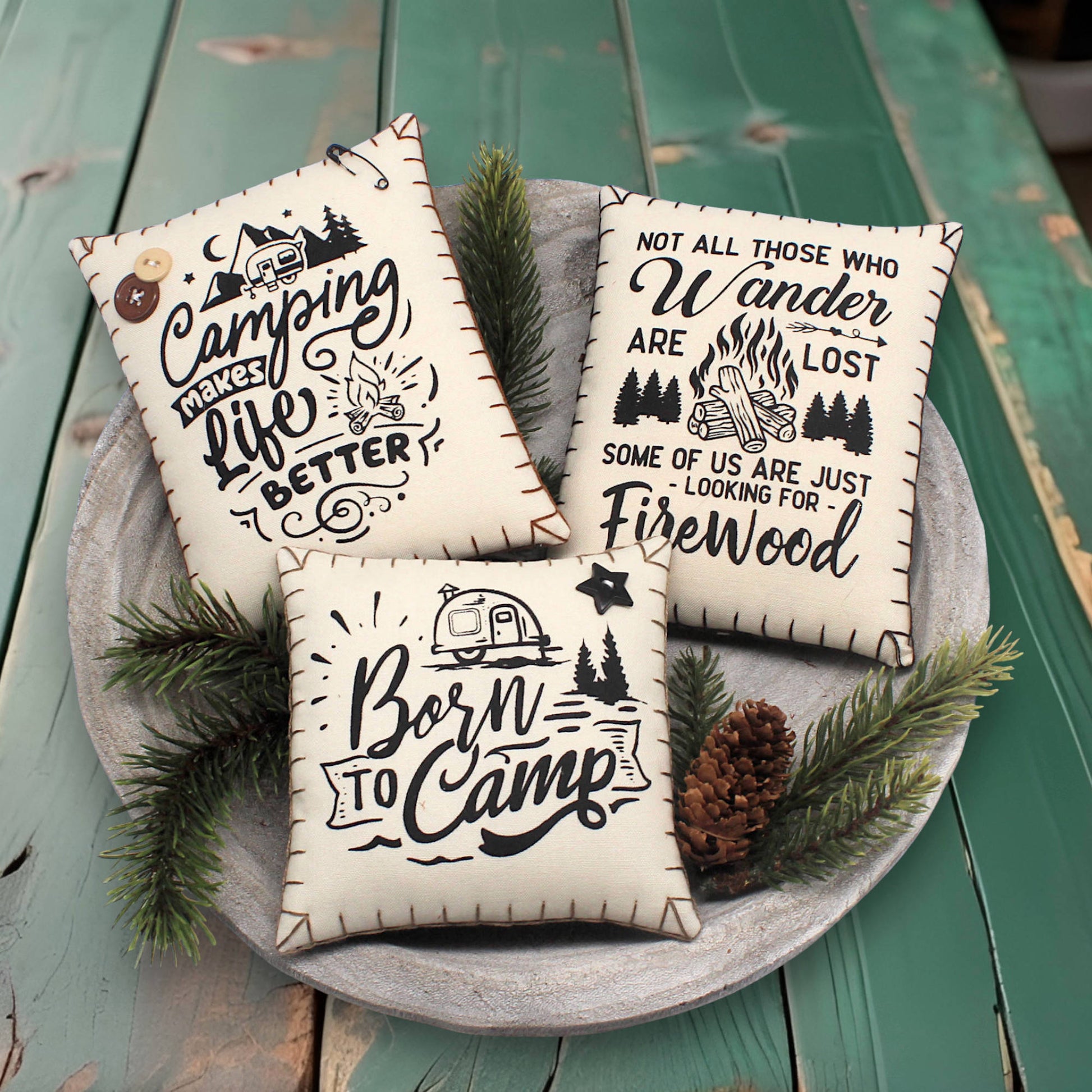 Three decorative pillows with camping-themed text on a wooden surface.