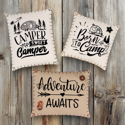 Three decorative signs with camping-themed text on a wooden background
