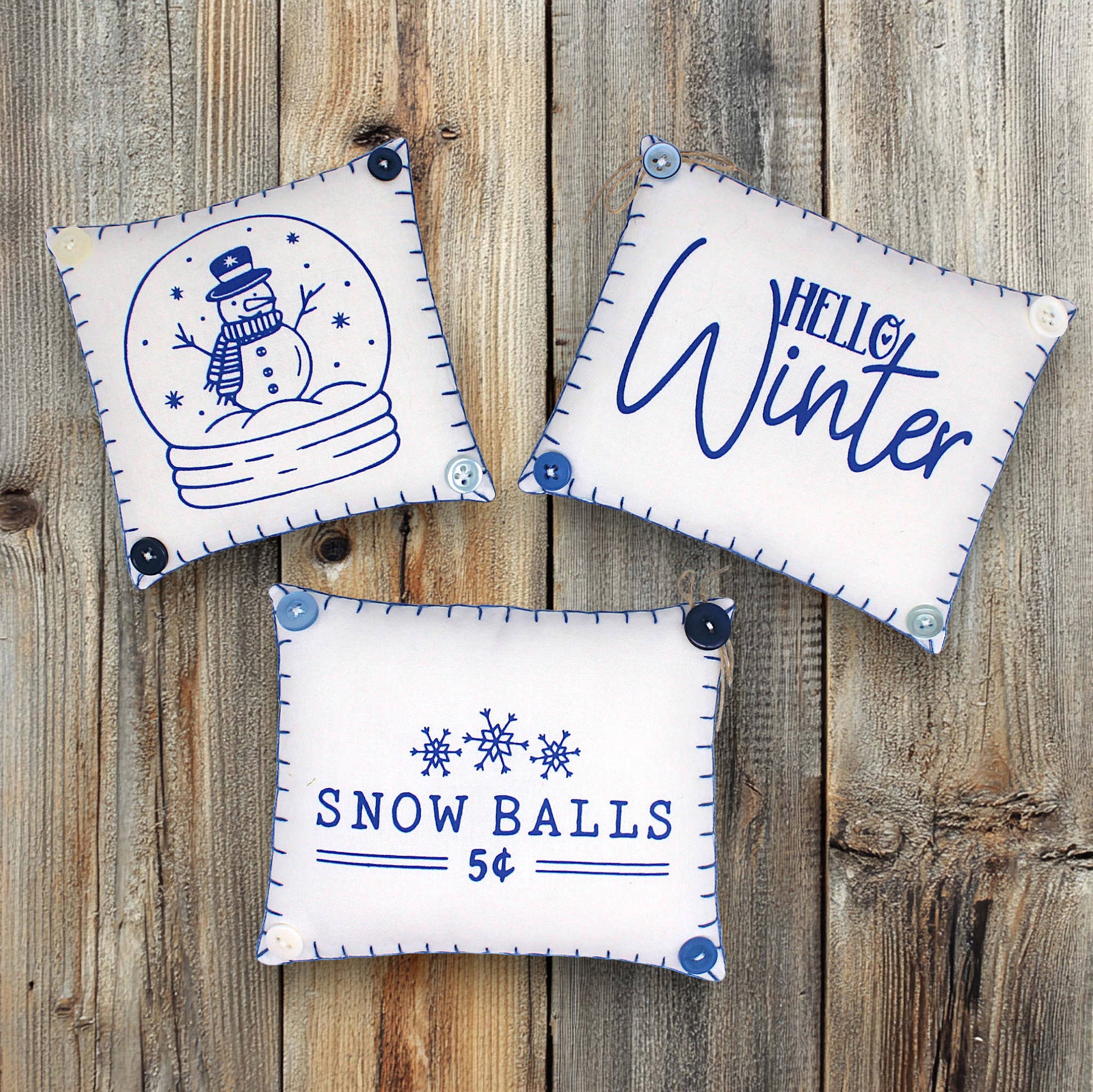 Three decorative pillows with winter-themed designs on a wooden surface