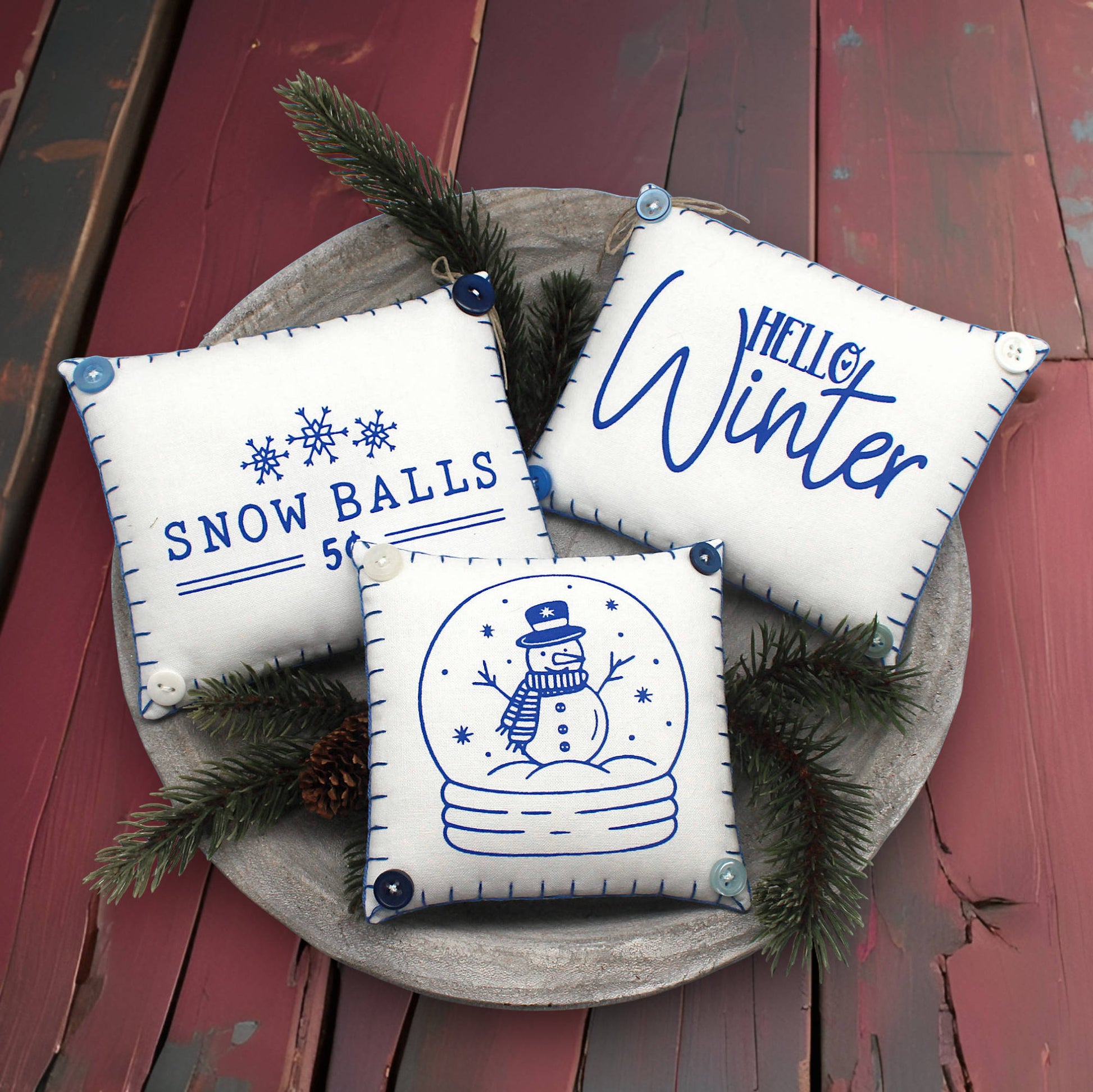 Three decorative pillows with winter-themed designs on a wooden surface.