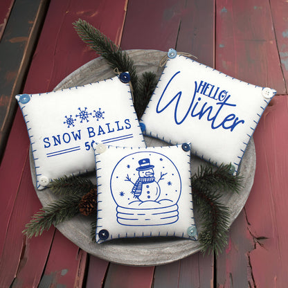 Three decorative pillows with winter-themed designs on a wooden surface.