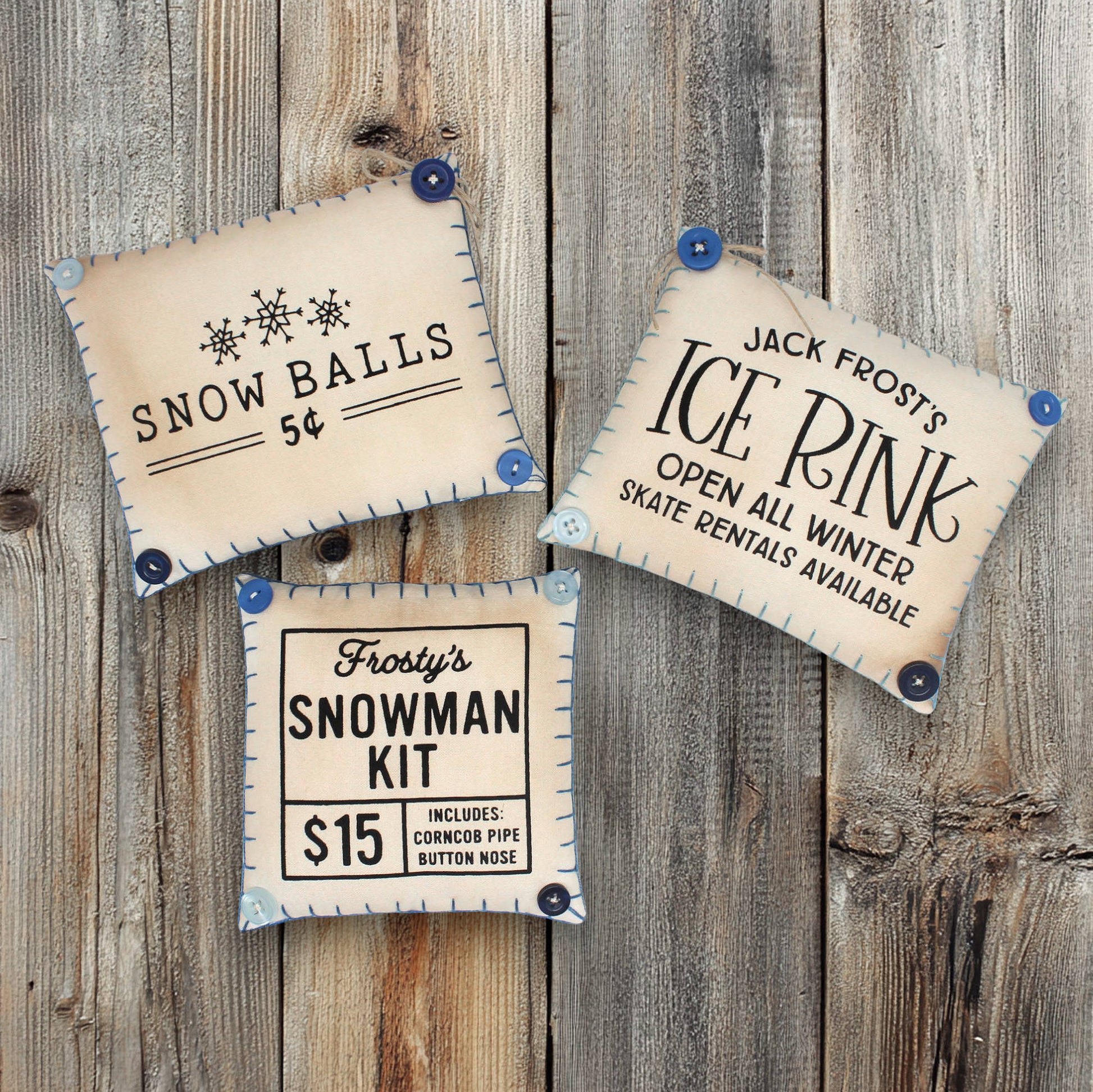 Three vintage-style mini pillow bowl fillers on a wooden background, advertising 'Snow Balls', 'Jack Frost's Ice Rink', and 'Frosty's Snowman Kit'.